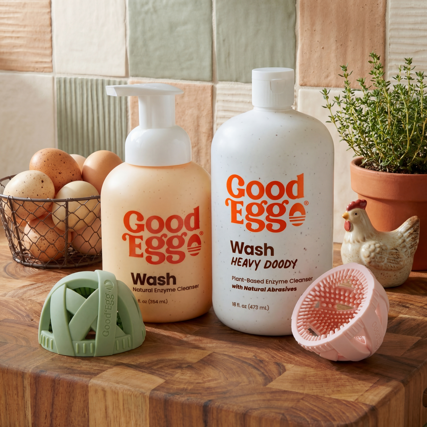 Two bottles of GoodEgg wash on a wooden surface with GoodEgg Brushes and kitchen items in the background.