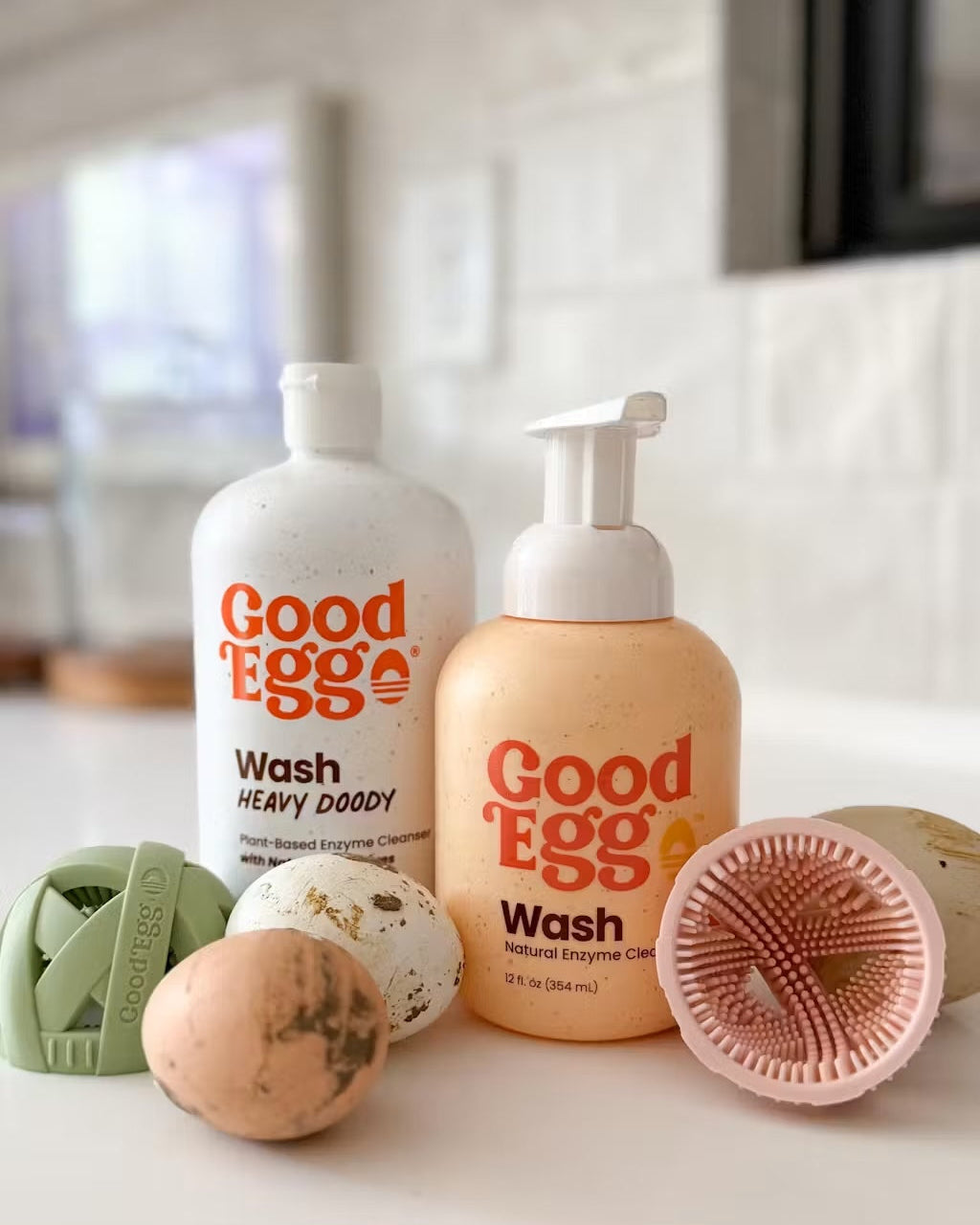 Two bottles of 'Good Egg' wash on a white surface with dirty eggs and GoodEgg brushes.